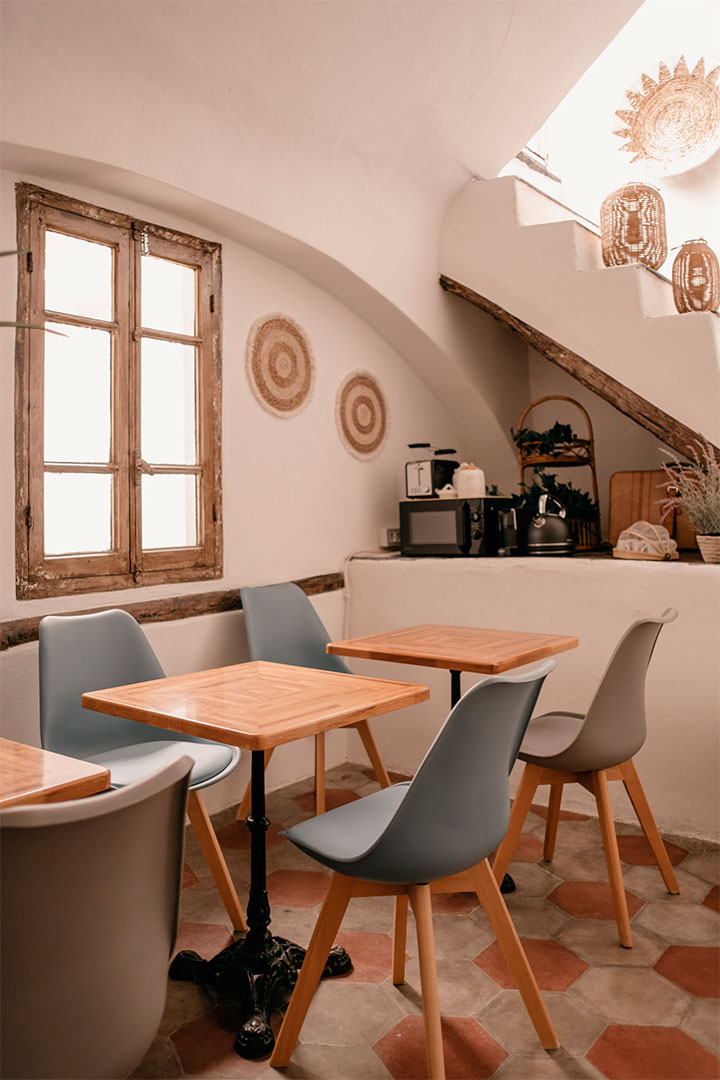 The shared kitchen with wooden tables, blue chairs, and cement tiles on the floor at the Ensemble Rooms guesthouse in Alassio.