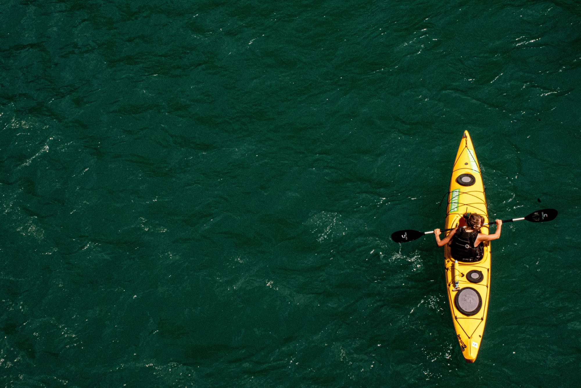 A zenithal shot of a person sailing in the sea with a yellow kayak