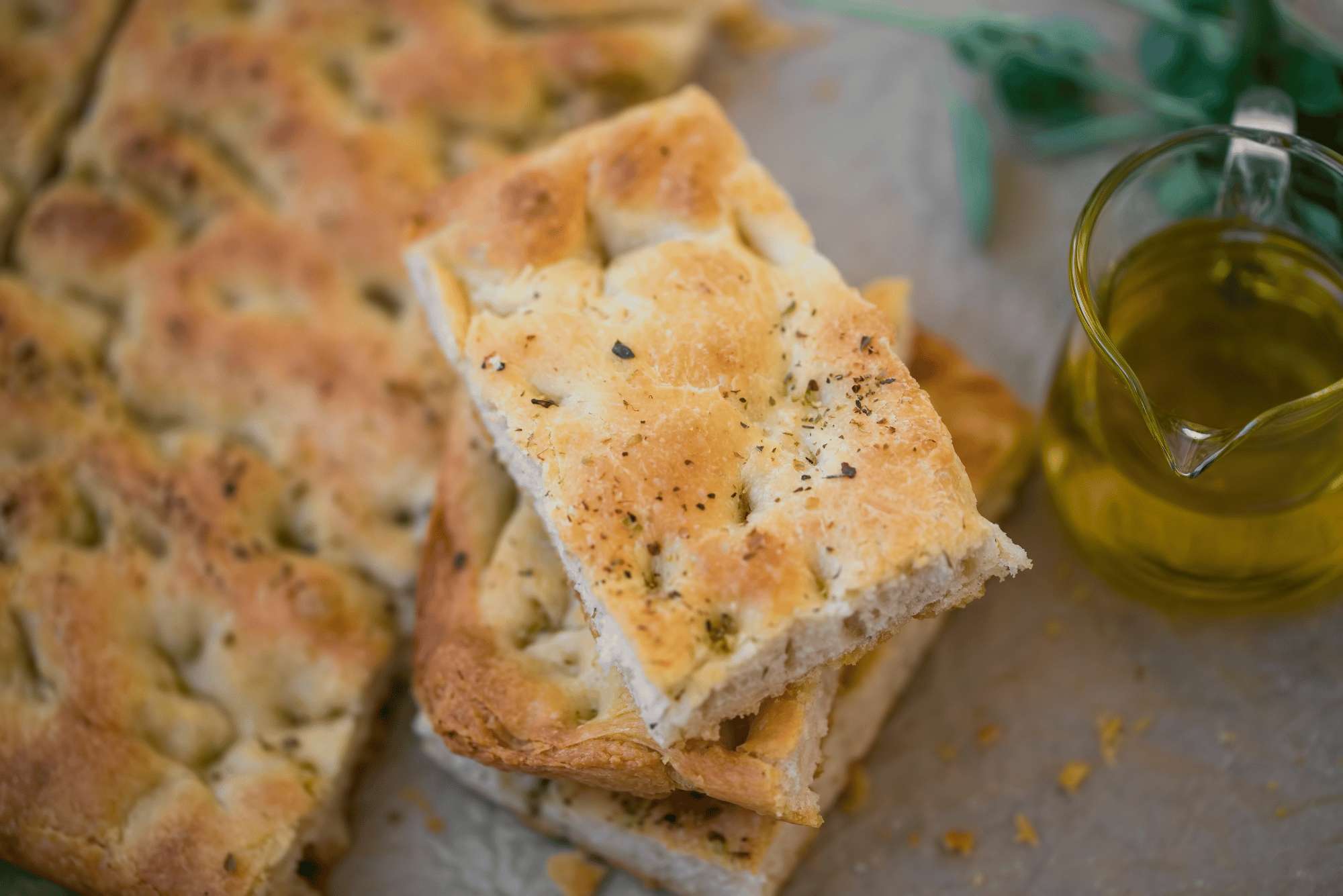 Delle fette di focaccia bianca con rosmarino e accanto una oliera