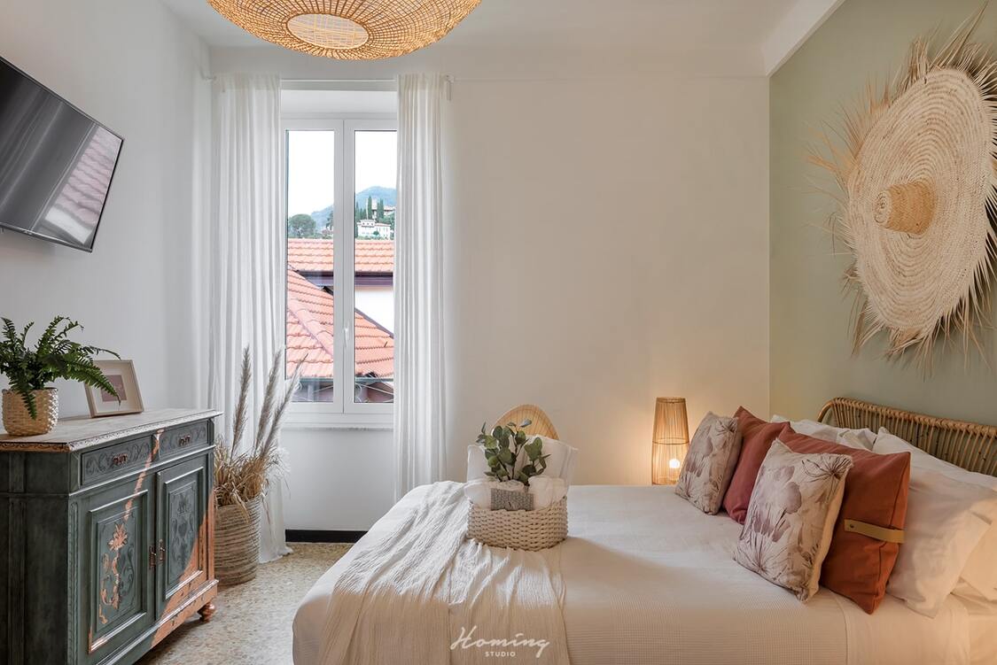 The bright Giselle double bedroom in Alassio with bed, white French window and large straw hat hanging above the headboard