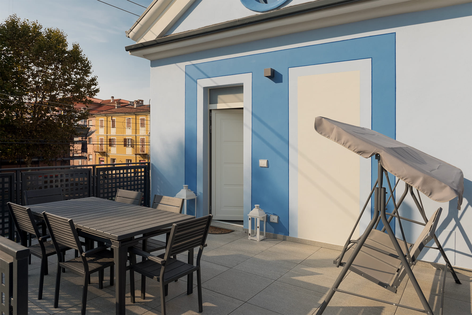 The large terrace on the first floor of the blue house, with its distinctive pointed roof and round window, furnished with a table, chairs, and a rocking chair, offers tranquility in Savigliano... before setting off again for the next destination.